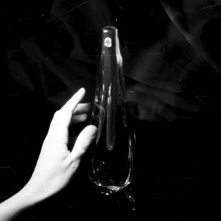 Here's a brief summary of the image: Hand holds a clear, elongated glass vessel in darkness.