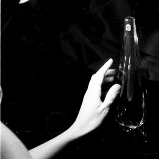 Here's a brief summary of the image: Hand holds a clear, elongated glass vessel in darkness.