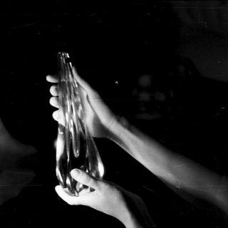 Hands hold a glass bottle in a dark space.
