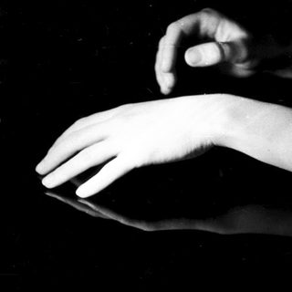 Here's a brief summary of the image: Hand making a gesture reflected in a dark surface.