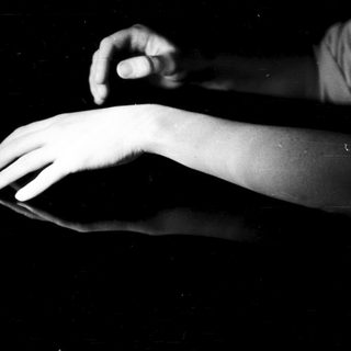 Here's a brief summary of the image: Hand making a gesture reflected in a dark surface.