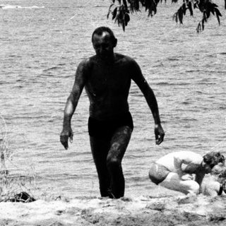 Here's a brief summary of the image: Three figures near a lake, appearing to be enjoying a day outdoors.