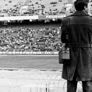 Men overlook a stadium filled with a large crowd.
