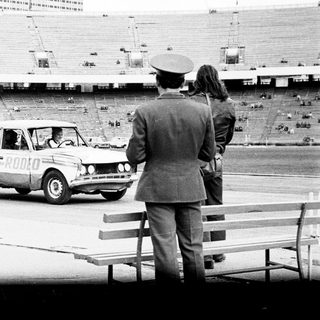 Officials observe a car driving across an empty stadium.