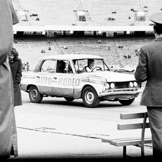 Officials observe a car driving across an empty stadium.