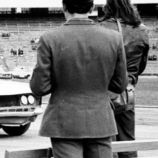 Officials observe a car driving across an empty stadium.