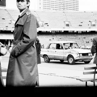 Officials observe a car driving across an empty stadium.