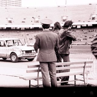Officials observe a car near an empty stadium.