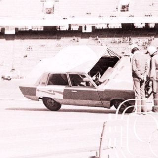 Men near a car in a stadium, possibly during an event.