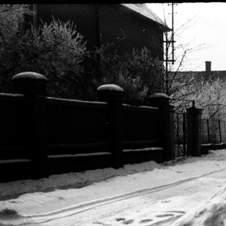 Snow-covered road with footprints and a fence in the distance.