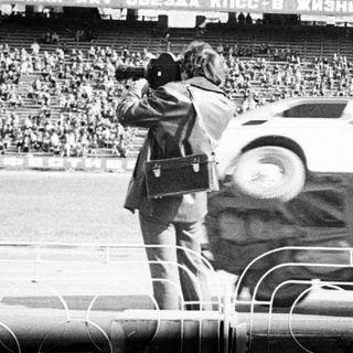Man stands atop overturned car in stadium during event.