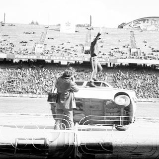 Man performs acrobatics on an overturned car in stadium.