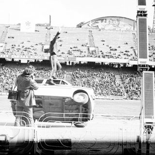 Man performs acrobatics on an overturned car in stadium.