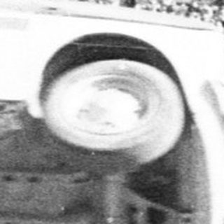 Man performs acrobatics on an overturned car in stadium.