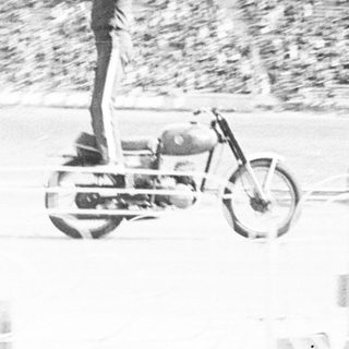 Man stands on motorcycle in an empty stadium.