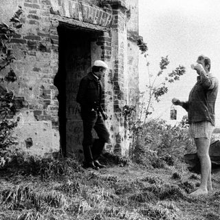 Two men near a ruined building by a body of water.