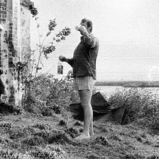 Two men near a ruined building by a body of water.