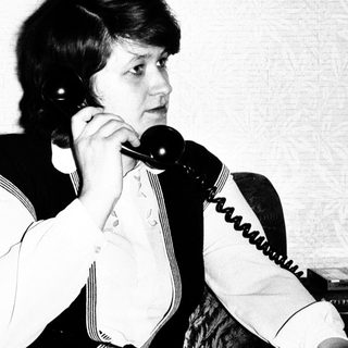 Here's a brief summary of the image: Woman on a vintage telephone, seated on a sofa.