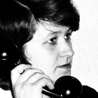 Here's a brief summary of the image: Woman on a vintage telephone, seated on a sofa.