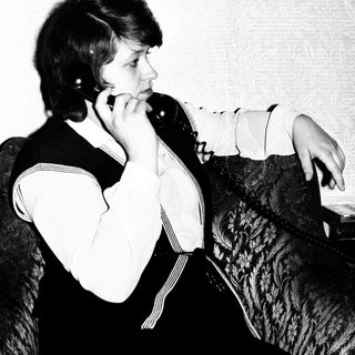 Woman seated, holding a vintage telephone to her ear.