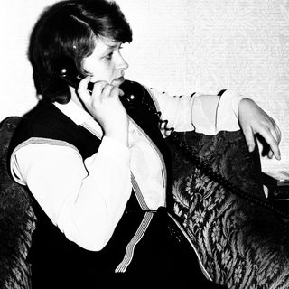 Woman seated, holding a vintage telephone to her ear.