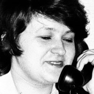 Woman sits, holding a telephone, in a vintage setting.