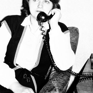Here's a brief summary of the image: Woman seated, holding a vintage telephone to her ear.