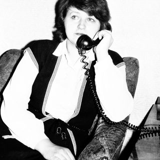 Here's a brief summary of the image: Woman seated, holding a vintage telephone to her ear.