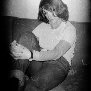 Here's a brief summary of the image: Woman seated, looking down, with visible vintage film grain.