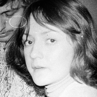 Here's a brief summary of the image: A couple stands close together in a dimly lit room.