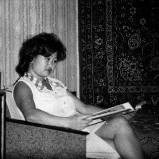 Woman seated, reading in a room with vintage furnishings.