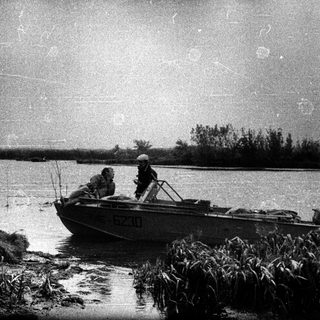 Three people in a boat near a waterfront.