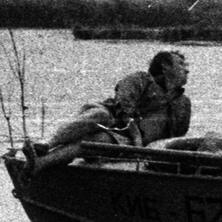 Three people in a boat near a waterfront.