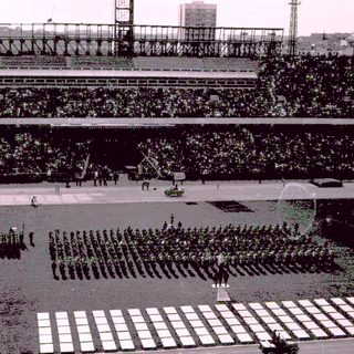 Military parade taking place in a large stadium.