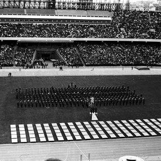 Ceremonial parade in a large, crowded stadium.