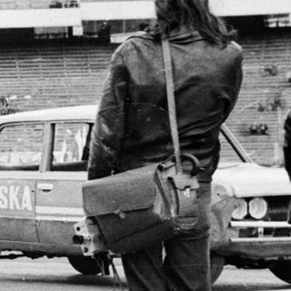 Cars drive past an empty stadium; people watch.