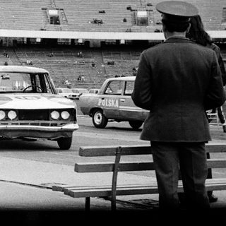 People near cars and stadium, possibly under surveillance.