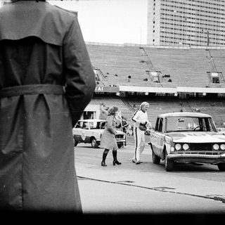 People near cars and stadium, possibly under surveillance.