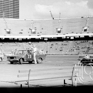 Man performing a stunt involving a car in a stadium.