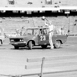 Man performing a stunt involving a car in a stadium.