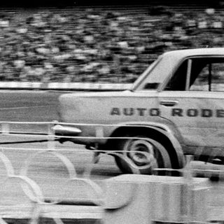 Truck at an auto rodeo event with a blurred stadium backdrop.