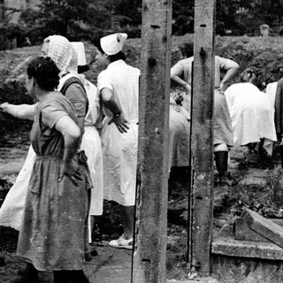 Here's a brief summary of the image: Women in uniforms observe an excavation site outdoors.