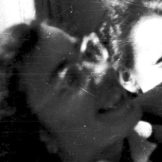 Two people resting closely on a bed near a window.