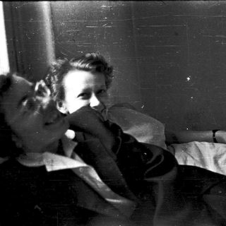 Two people resting closely on a bed near a window.