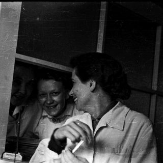 Two women laughing indoors near open window.