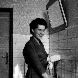 Person smiling while holding a suitcase in hallway.