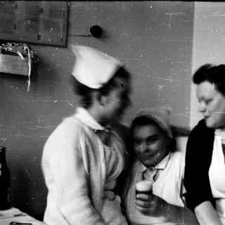 Nurses in 1940s-50s uniforms drinking together indoors.