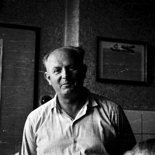 Old man standing indoors near cinema poster.