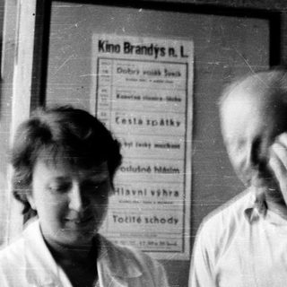Two people standing indoors near a cinema poster.