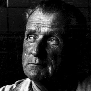 A solemn, weathered man in dim lighting.